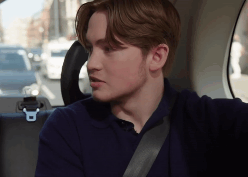 A Young Man Is Sitting In The Back Seat Of A Car With A Seat Belt Around His Neck GIF