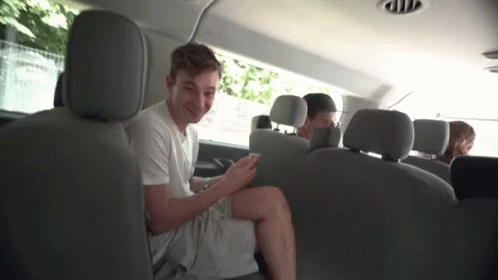 A Young Man Is Sitting In The Back Seat Of A Van Looking At His Cell Phone . GIF