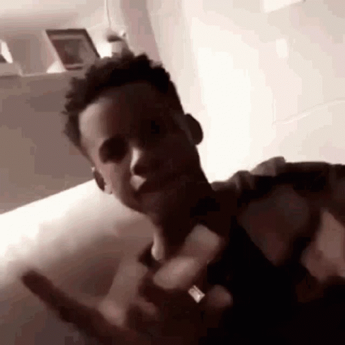 A Young Man Is Sitting On A Bed Making A Funny Face . GIF