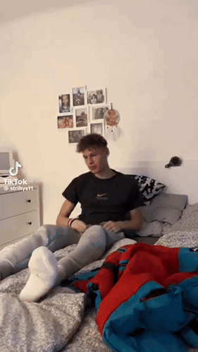 A Young Man Is Sitting On A Bed Wearing White Socks And Jeans . GIF