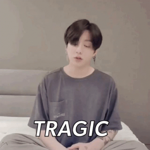 A Young Man Is Sitting On A Bed With His Eyes Closed And The Word Tragic On His Shirt GIF