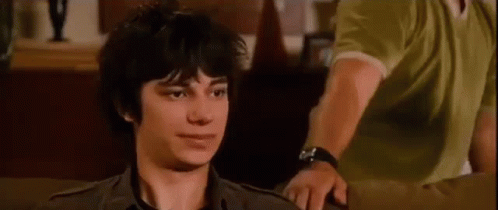 A Young Man Is Sitting On A Couch And Looking At The Camera . GIF
