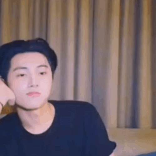 A Young Man Is Sitting On A Couch In Front Of A Window . GIF