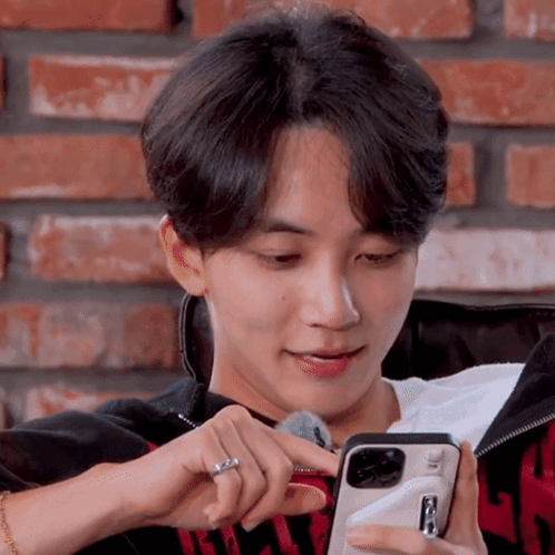 A Young Man Is Sitting On A Couch Looking At A Cell Phone GIF
