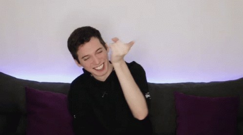 a young man is sitting on a couch with purple pillows and smiling