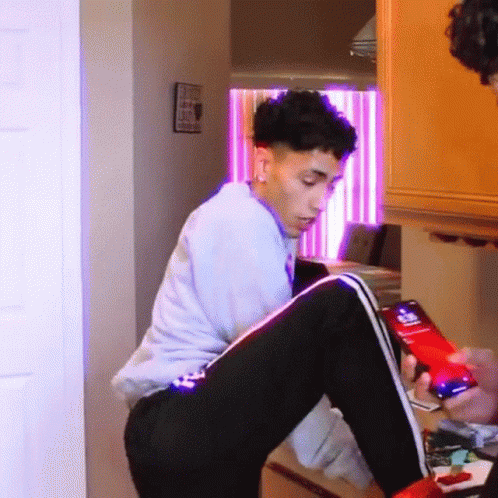 A Young Man Is Sitting On A Table Looking At A Cell Phone . GIF