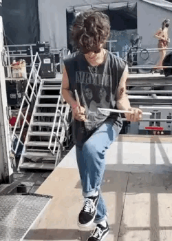 A Young Man Is Sitting On A Wooden Platform Holding A Drum Stick . GIF