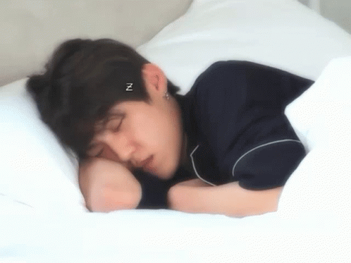 A Young Man Is Sleeping On A Bed With A Headband That Says ` ` N ` ` On It . GIF