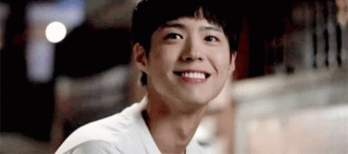 A Young Man Is Smiling And Looking At The Camera While Sitting At A Table . GIF