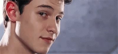 A Young Man Is Smiling And Looking At The Camera With A Blue Background . GIF