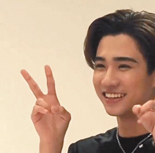 A Young Man Is Smiling And Making A Peace Sign With His Hand GIF