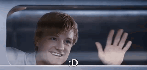 a young man is smiling and waving his hand while looking out of a window .