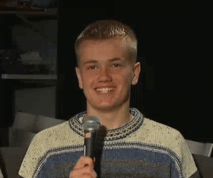 A Young Man Is Smiling While Holding A Microphone In His Hand . GIF