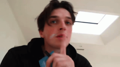 A Young Man Is Smoking A Cigarette In A Room With A Skylight . GIF