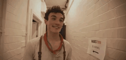 A Young Man Is Standing In A Hallway Next To A Sign That Says Slowing . GIF