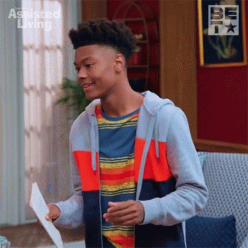 A Young Man Is Standing In A Living Room Holding A Piece Of Paper In His Hand . GIF