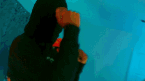 A Young Man Is Standing In A Room Wearing A Black Leather Jacket And A Red Hoodie . GIF
