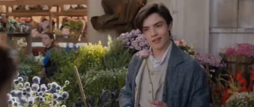 A Young Man Is Standing In Front Of A Bunch Of Flowers In A Flower Shop . GIF