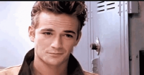 A Young Man Is Standing In Front Of A Locker And Looking At The Camera . GIF