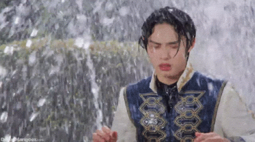 A Young Man Is Standing In Front Of A Waterfall . GIF