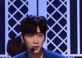 A Young Man Is Standing On A Stage Wearing A Microphone And A Blue Jacket . GIF