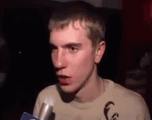 A Young Man Is Talking Into A Microphone While Making A Funny Face . GIF