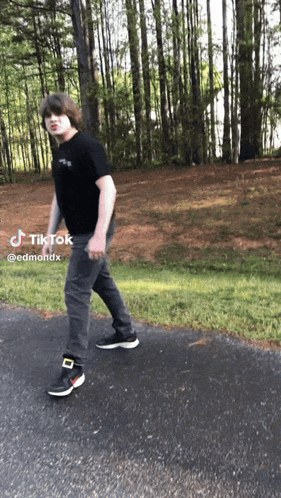 A Young Man Is Walking Down A Road With A Tiktok Sticker On The Bottom GIF