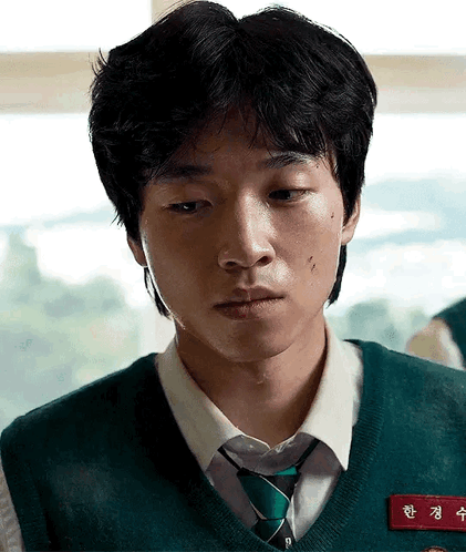 A Young Man Is Wearing A Green Vest And Tie And Has A Name Tag On His Chest . GIF