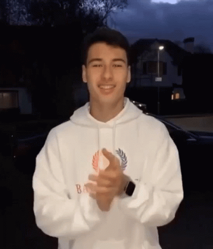 a young man is wearing a white hoodie and clapping his hands .