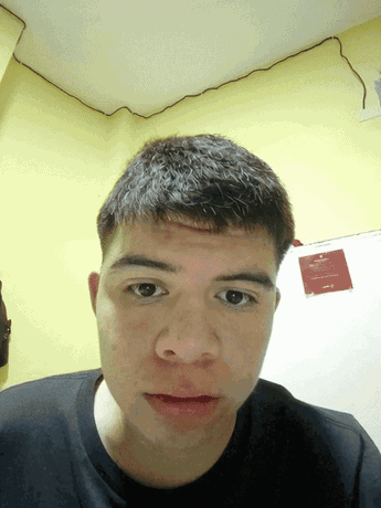 A Young Man Looks At The Camera In Front Of A Yellow Wall With A Sign That Says " No Smoking " On It GIF