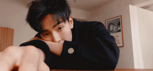 A Young Man Rests His Head On His Arm In Front Of A Framed Picture That Says Oa GIF