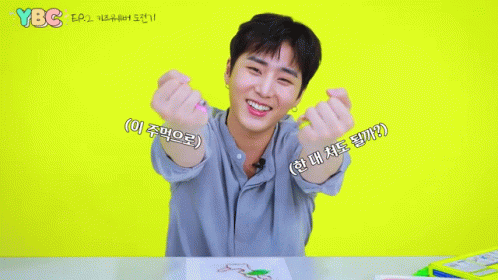 A Young Man Sitting At A Table With His Hands In The Shape Of A Heart And Ybc Written On The Yellow Background GIF
