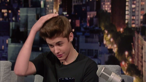 A Young Man Sitting In Front Of A Microphone With His Hand On His Hair GIF
