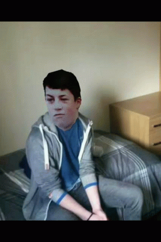A Young Man Sitting On A Bed With A Picture Of His Face On His Chest GIF