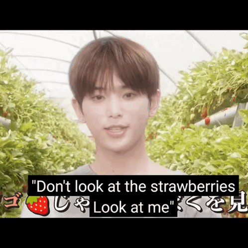 A Young Man Stands In Front Of A Greenhouse With Strawberries Hanging From The Ceiling GIF
