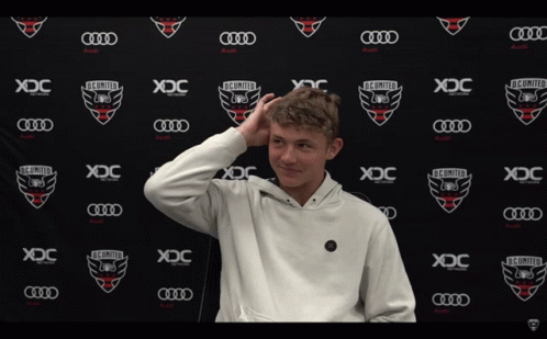 A Young Man Stands In Front Of A Wall That Says Xdc On It GIF