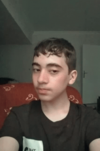 A Young Man Taking A Selfie With A Black Shirt And A Red Couch In The Background GIF