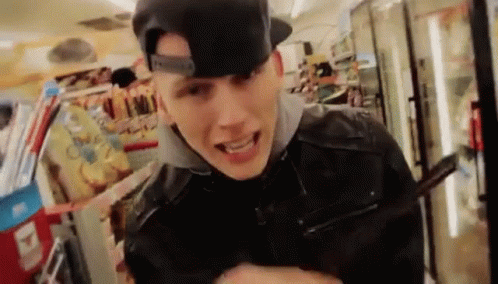 A Young Man Wearing A Baseball Cap And A Leather Jacket Is Standing In A Store . GIF