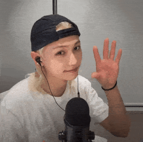 a young man wearing a baseball cap and headphones is waving at the camera .