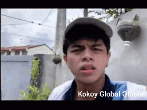 A Young Man Wearing A Baseball Cap Is Making A Funny Face With The Words Kokoy Global Official Written Below Him GIF