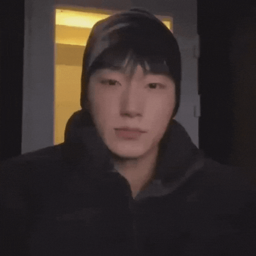 A Young Man Wearing A Beanie Looks At The Camera In A Dark Room GIF