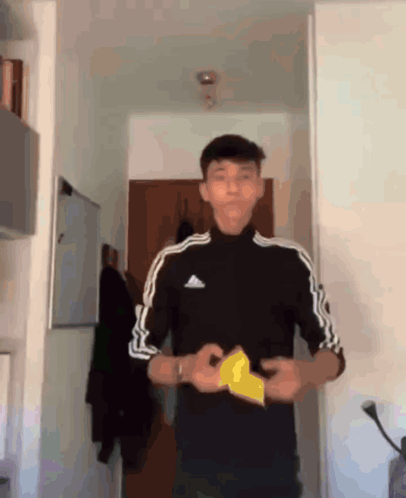 A Young Man Wearing A Black Adidas Shirt Holds A Piece Of Paper In His Hands GIF