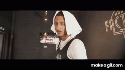 A Young Man Wearing A Black And White Basketball Jersey And A White Hooded Jacket Is Standing In A Room . GIF