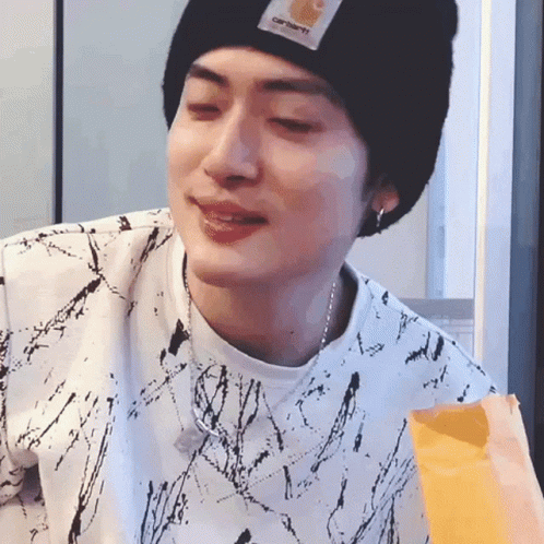A Young Man Wearing A Black Beanie And A White Shirt Is Eating A Bag Of French Fries . GIF