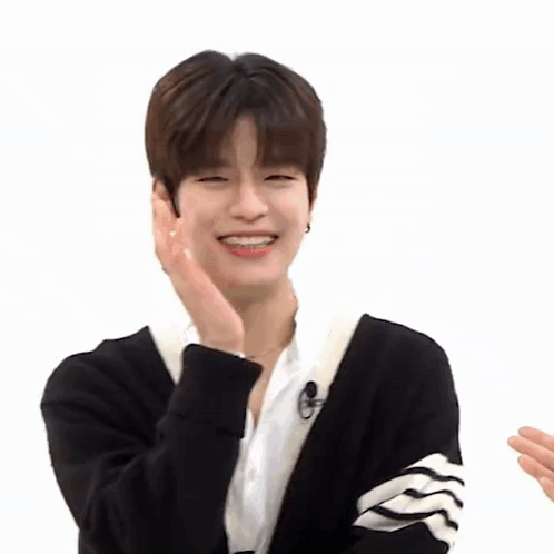 A Young Man Wearing A Black Cardigan And A White Shirt Is Smiling While Holding His Hand To His Face . GIF