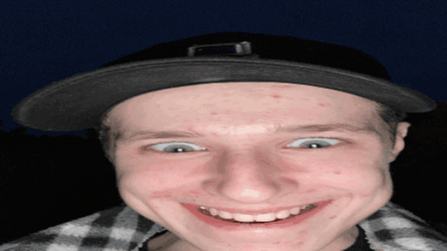 A Young Man Wearing A Black Hat And Plaid Shirt Smiles For The Camera GIF