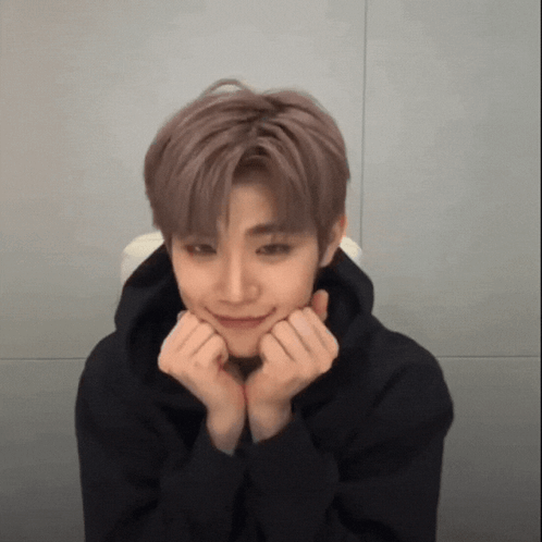 A Young Man Wearing A Black Hoodie Is Making A Face With His Hands On His Chin . GIF