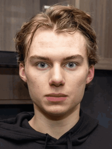 A Young Man Wearing A Black Hoodie Looks At The Camera With A Serious Look On His Face GIF