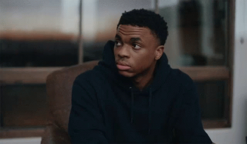 A Young Man Wearing A Black Hoodie Sits In A Chair GIF