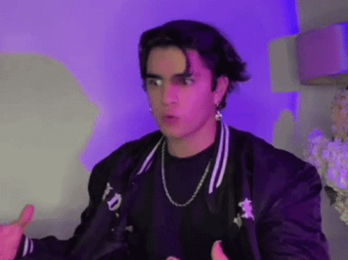 A Young Man Wearing A Black Jacket And A Necklace Is Giving A Thumbs Up Sign . GIF